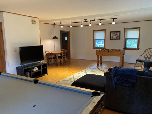 A living room with a pool table, a television, a dining area, and a foosball table.