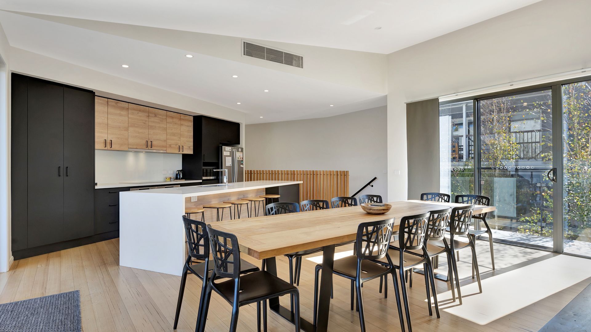 A modern kitchen with dark cabinetry, a central island, and a dining area with a large table and chairs.
