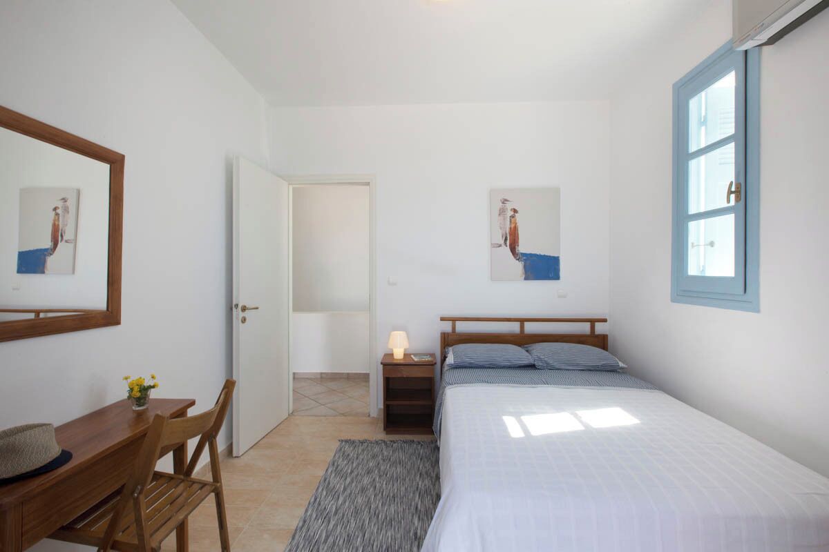 Un dormitorio con cama, mesita de noche, lámpara y un escritorio con silla.