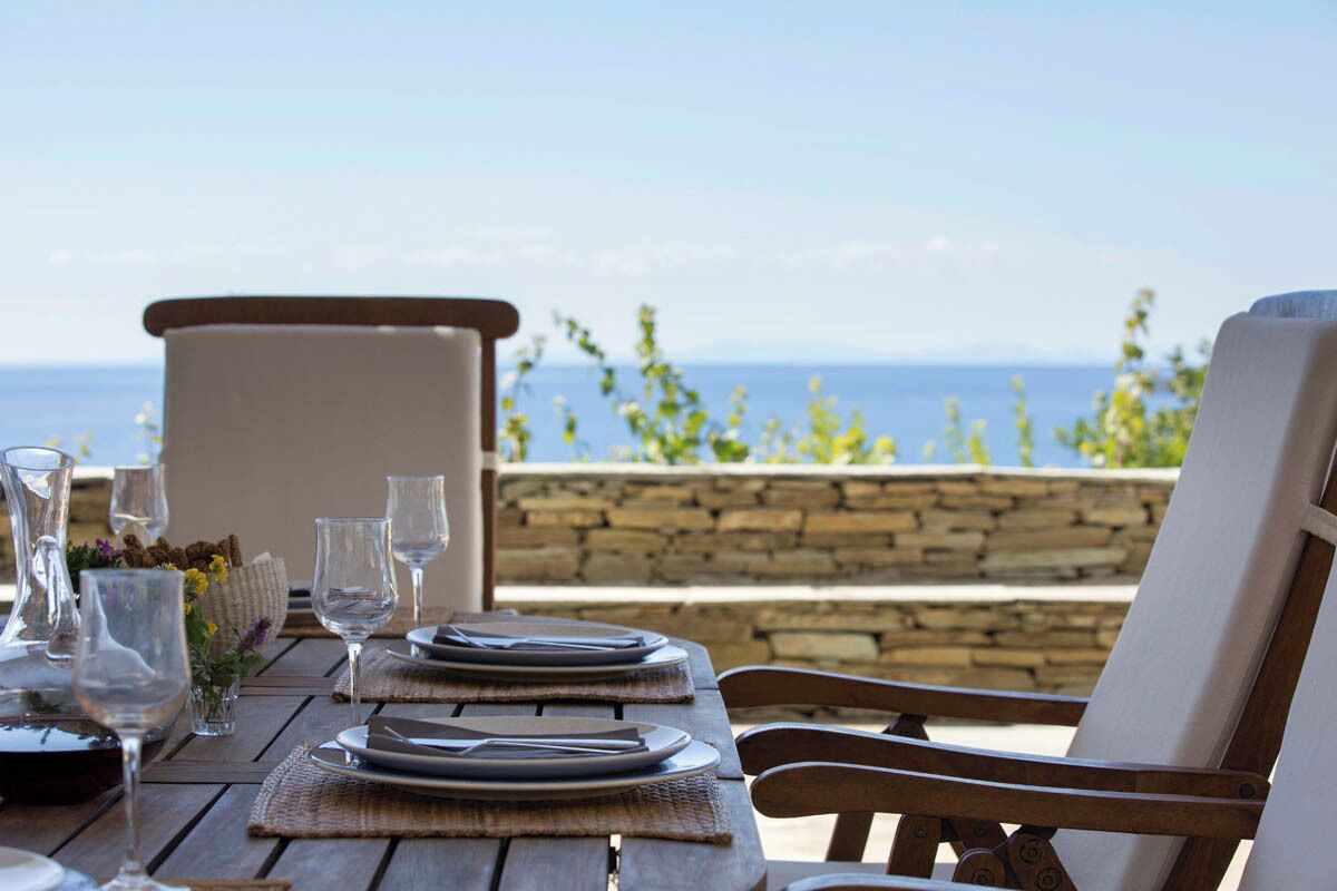 A wooden table set for dining with a view of the sea.