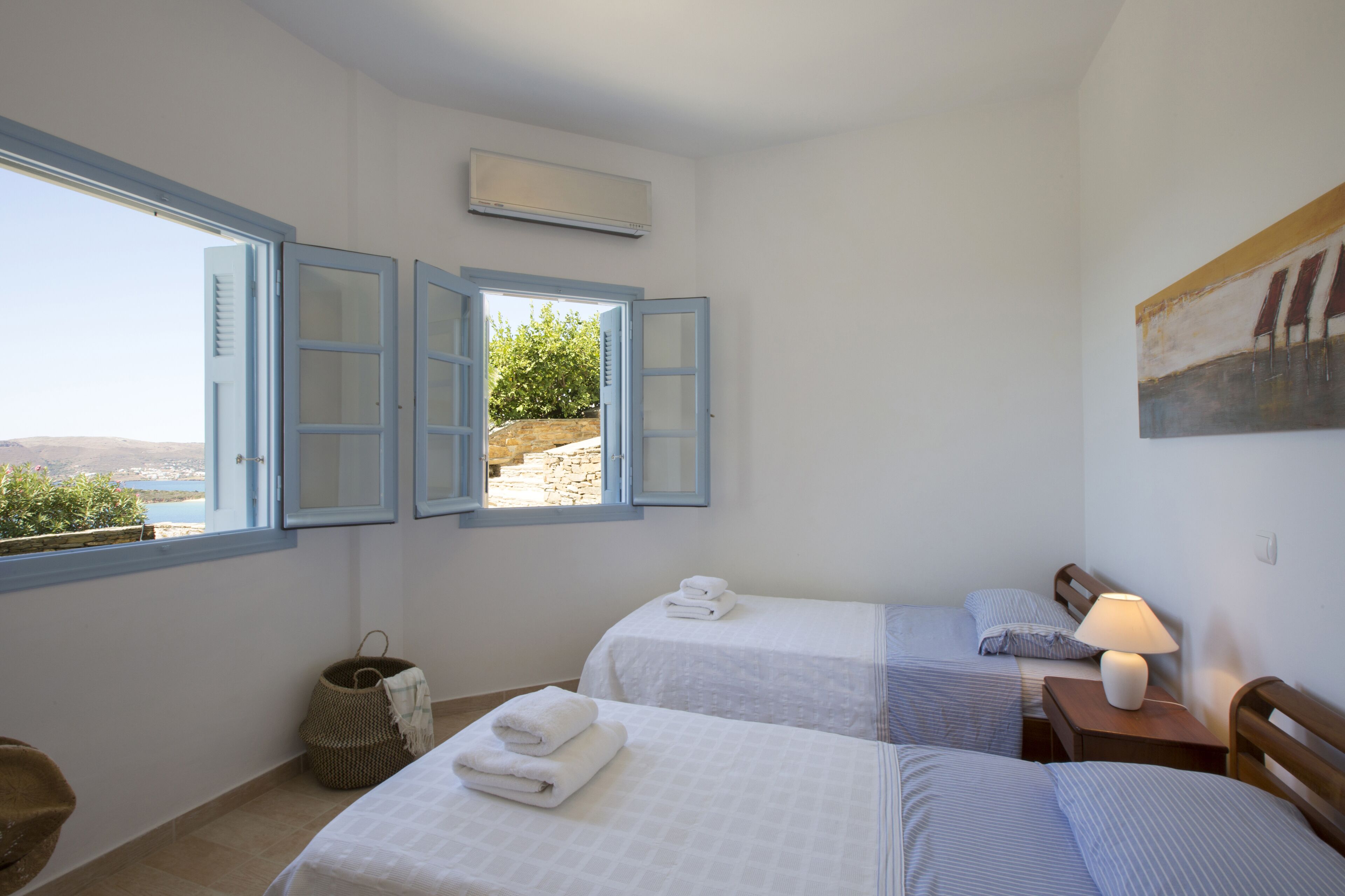 A bedroom with two beds, a window with blue shutters, a wall-mounted air conditioner, and a painting.