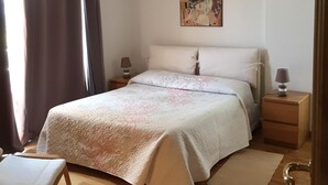 A bedroom with a bed, bedside tables, a chair, a painting on the wall, and a window with curtains. - Villa Asia, Holiday home (Massa Lubrense)