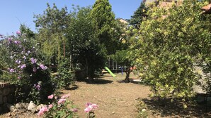 A garden with various plants and flowers, a playground with a slide, and a building in the background. - Villa Asia, Holiday home (Massa Lubrense)