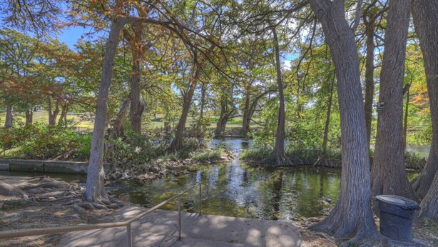 A serene park with a small pond, surrounded by trees and a concrete walkway. - Riviera | Pools & Hot-Tubs | Pet-Friendly* | King Bed (New Braunfels)