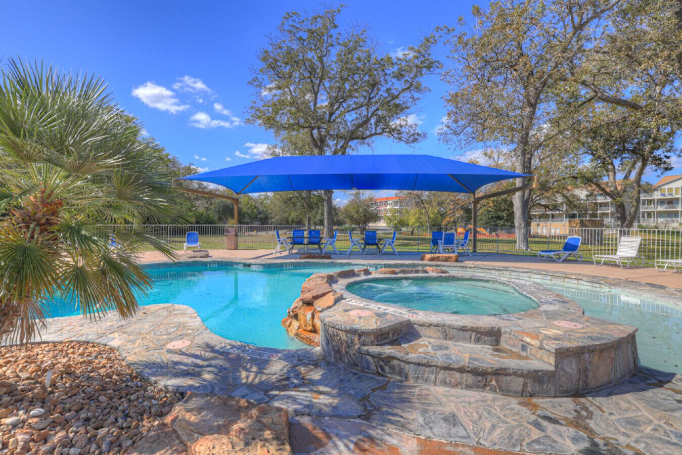 A swimming pool with a hot tub, surrounded by stone steps and a blue canopy.