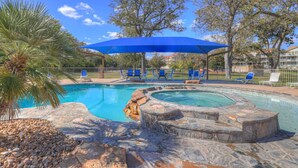 A swimming pool with a hot tub, surrounded by stone steps and a blue canopy. - Riviera | Pools & Hot-Tubs | Pet-Friendly* | King Bed (New Braunfels)