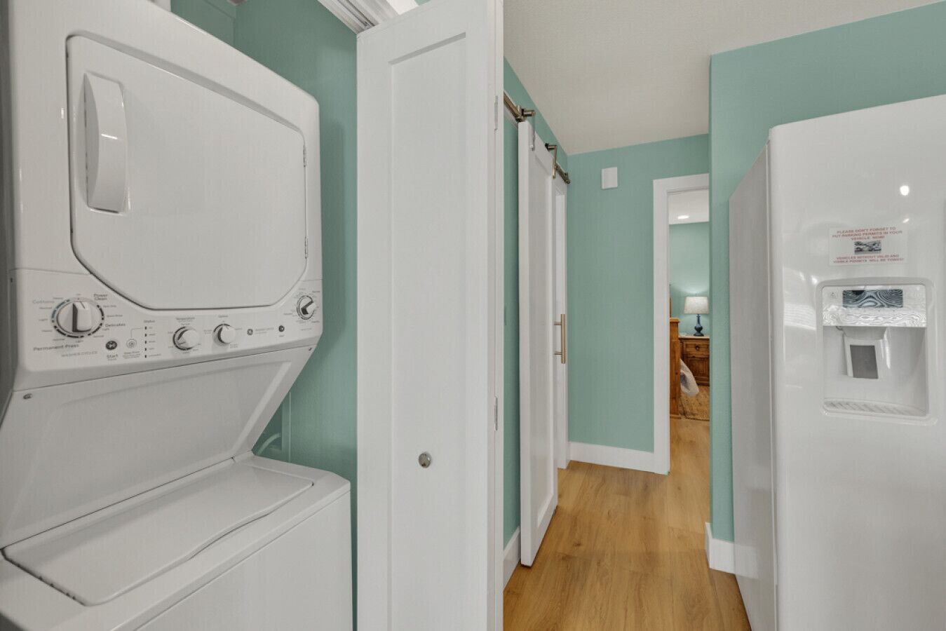 A laundry room with a front-loading washer and dryer, a water dispenser, and a hallway leading to a bedroom.