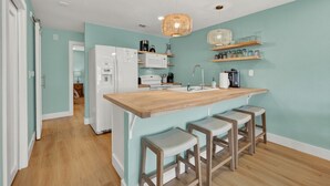A kitchen with a wooden island, bar stools, a refrigerator, a microwave, and a hanging light fixture. - Riviera | Pools & Hot-Tubs | Pet-Friendly* | King Bed (New Braunfels)