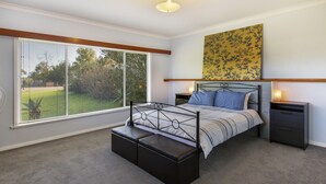 A bedroom with a bed, bedside tables, a bench, a large window, and a wall-mounted artwork.