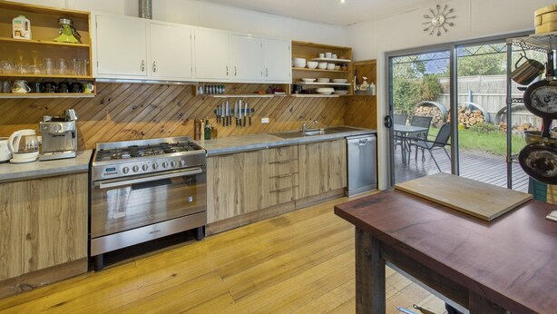 A modern kitchen with wooden cabinets, a stainless steel stove, and a dishwasher. There is a wooden countertop with various kitchen items and a view of the outdoor patio.