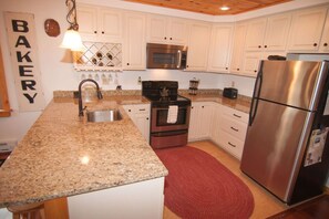 A kitchen with white cabinets, granite countertops, stainless steel appliances, and a red rug.