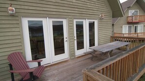 A wooden deck with a picnic table and chairs, a sliding glass door, and a balcony with a railing. - Three Bears in the Valley - Hot Tub, Pet Friendly (Davis)