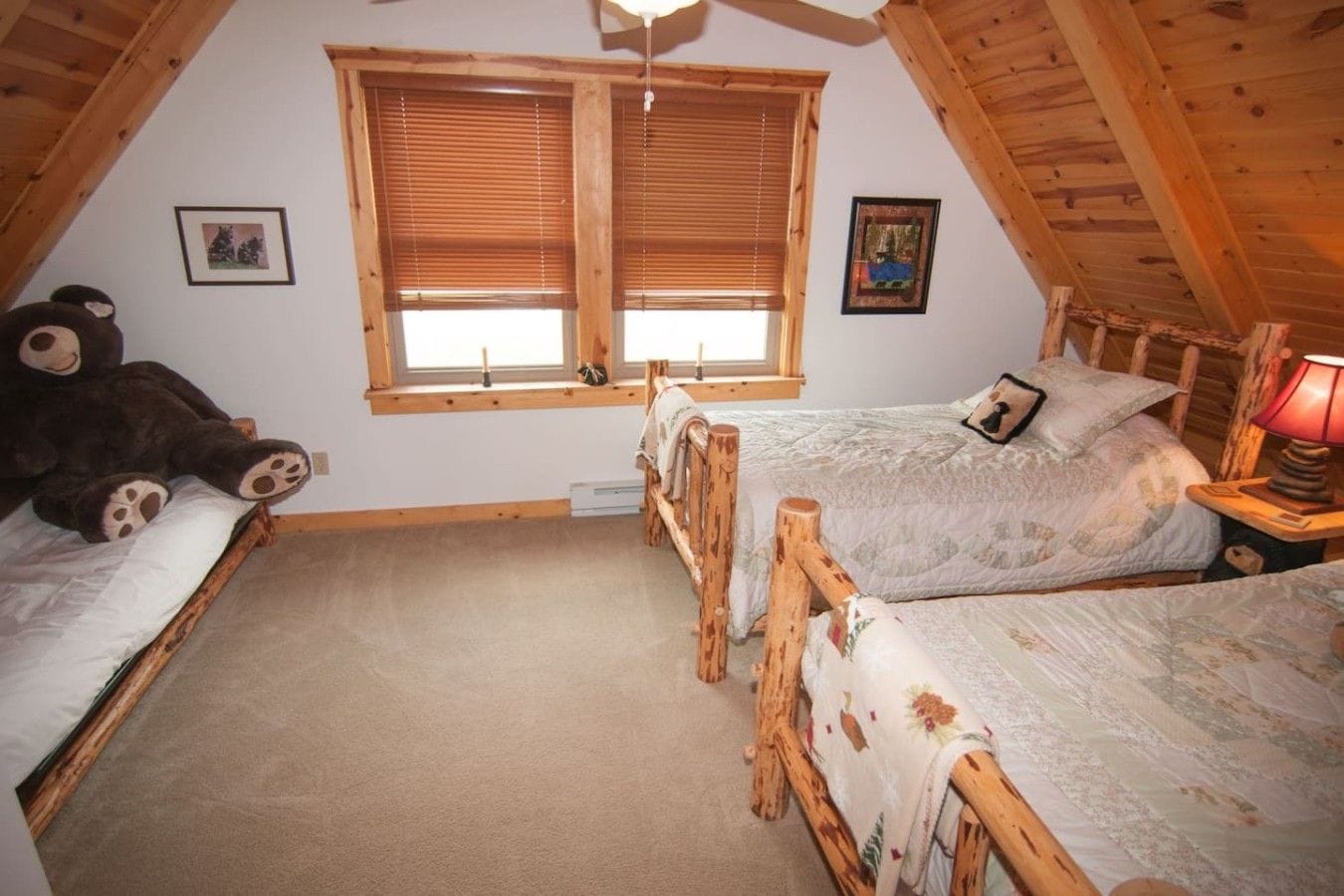 A bedroom with two wooden beds, a large teddy bear, and two windows with wooden blinds.