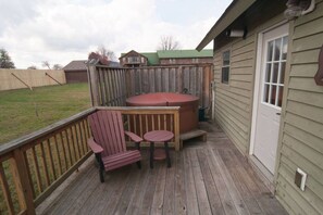 A wooden deck with a hot tub, a table, and two chairs.