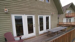 A wooden deck with a table and chairs, a sliding glass door, and a balcony with a railing. - Three Bears in the Valley (Davis)