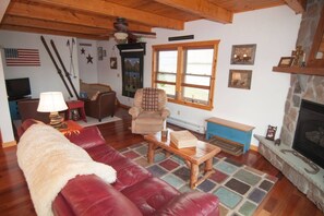 A cozy living room with a red leather sofa, a wooden coffee table, a fireplace, and a stone fireplace surround.