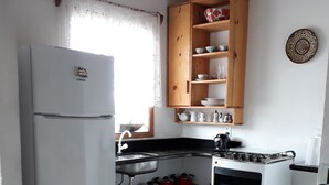 Kompakti keittiö, jossa on jääkaappi, liesi ja puiset hyllyt tiskialtaan yläpuolella.