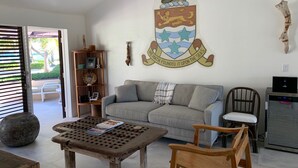 A living room with a grey sofa, a wooden coffee table, and a bookshelf. A coat of arms is displayed on the wall.