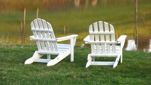 Deux chaises Adirondack blanches, placées au bord d’un lac paisible aux rives verdoyantes.