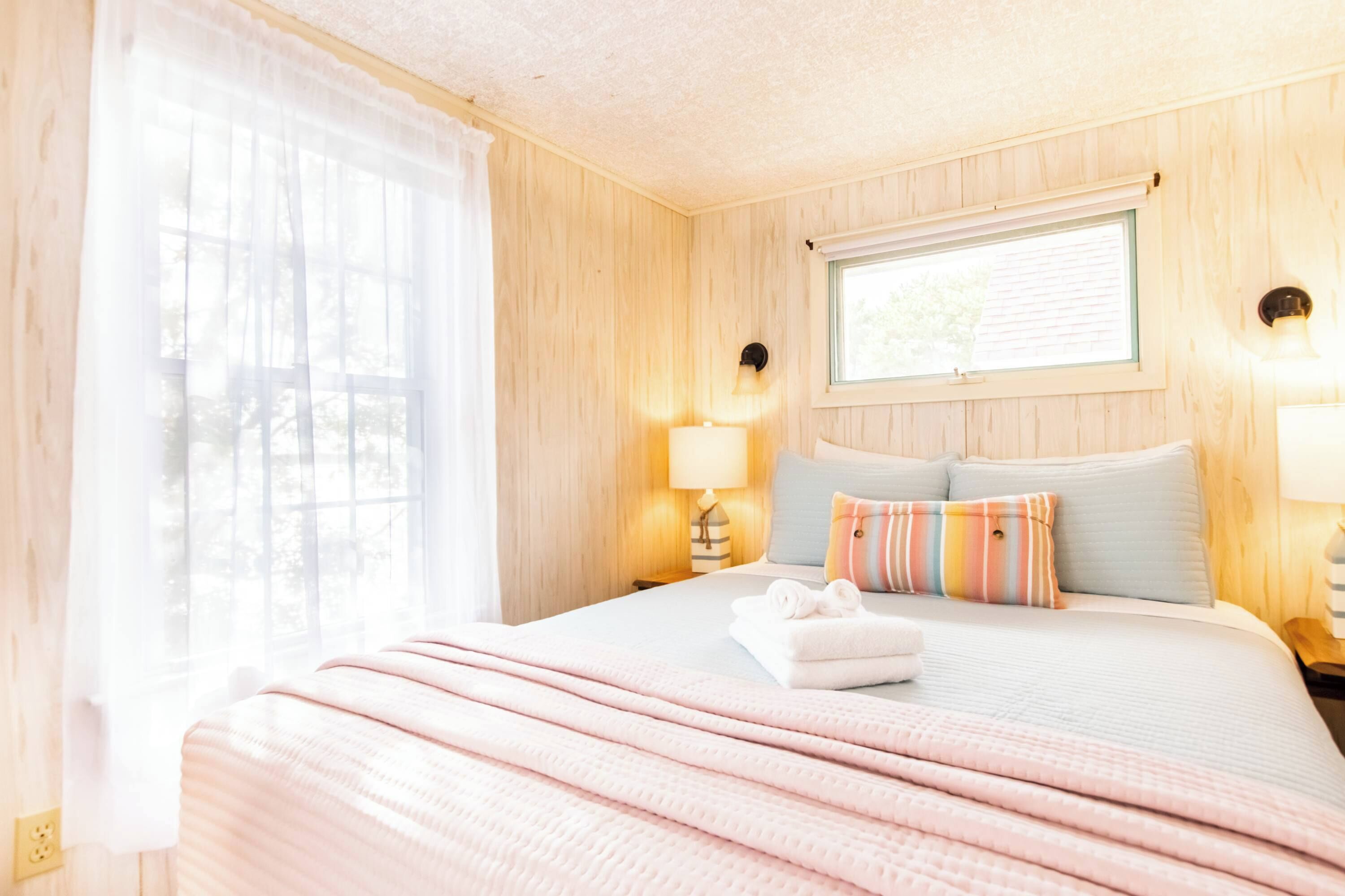 A hotel room with a bed, a window, and a nightstand with a lamp.