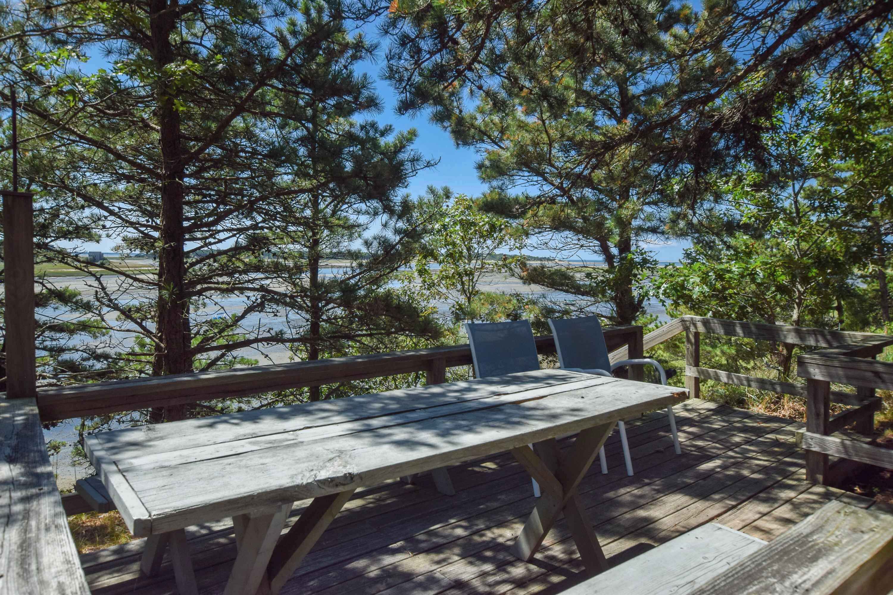A wooden deck with a table and chairs overlooking a body of water, surrounded by trees.