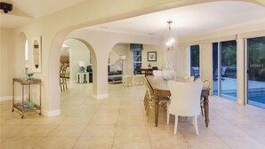 Un salón amplio con una mesa y sillas de comedor, una cocina al fondo y grandes puertas correderas de vidrio que dan a un espacio exterior.
