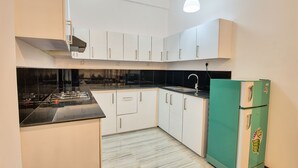 A compact kitchen with white cabinets, a black countertop, and a green refrigerator. - Ashiyana (Mirissa)