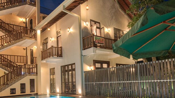 A multi-story hotel with a swimming pool, outdoor lighting, and a wooden fence. - Ashiyana (Mirissa)