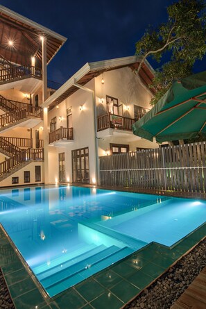 A multi-story hotel with a swimming pool, outdoor lighting, and a wooden fence. - Ashiyana (Mirissa)