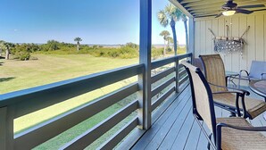 A covered outdoor area with a view of a grassy field and palm trees.