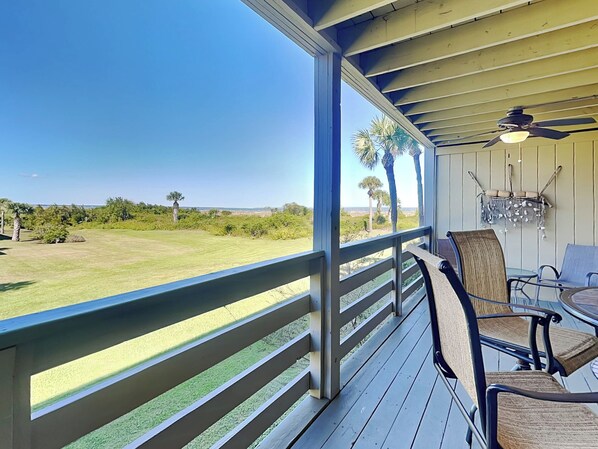 A covered outdoor area with a view of a grassy field and palm trees. - Upgraded & Spacious w/ Large Balcony & Idyllic Views + Community Pool, B (Tybee Island)