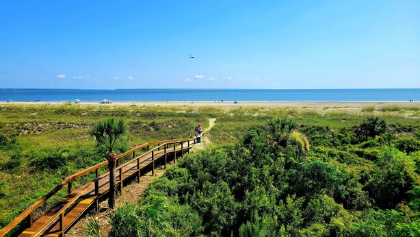 A wooden boardwalk leading to a beach with a clear view of the ocean and distant boats.