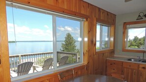 A wooden interior with large windows overlooking a lake, a dining table, and a kitchen area. - Cottage #10 - 3 bedroom/ 1 bath (Cape Vincent)