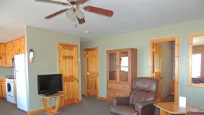 A living room with a television on a wooden stand, a leather armchair, and a small wooden table. - Cottage #10 - 3 bedroom/ 1 bath (Cape Vincent)