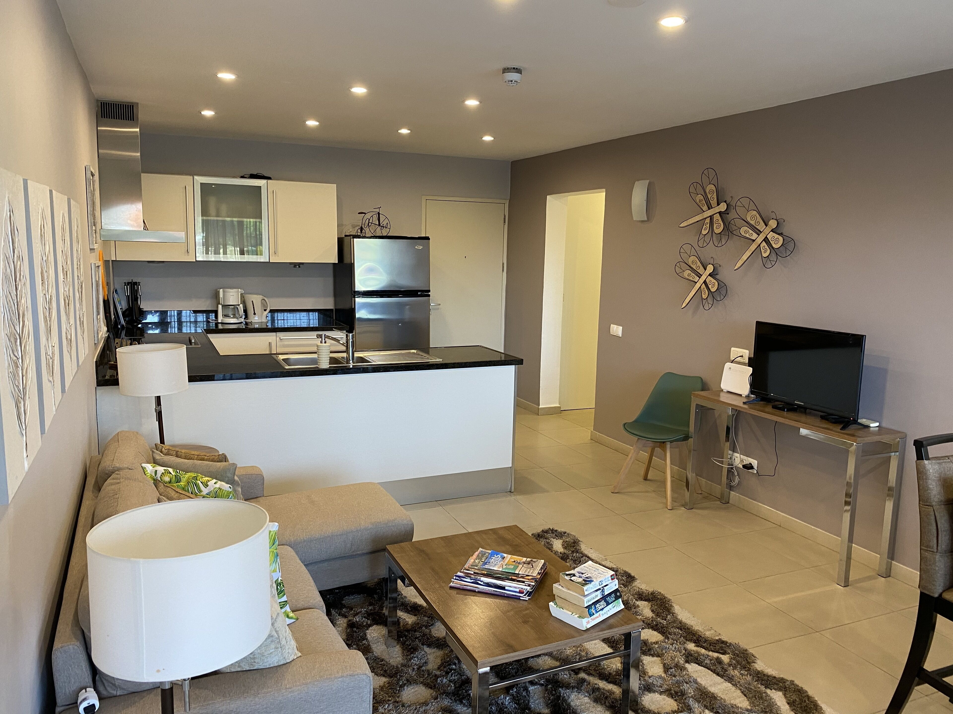 Un apartamento moderno con cocina, sala de estar y comedor. Cuenta con un sofá, una mesa de centro, un televisor y una pequeña mesa de comedor.