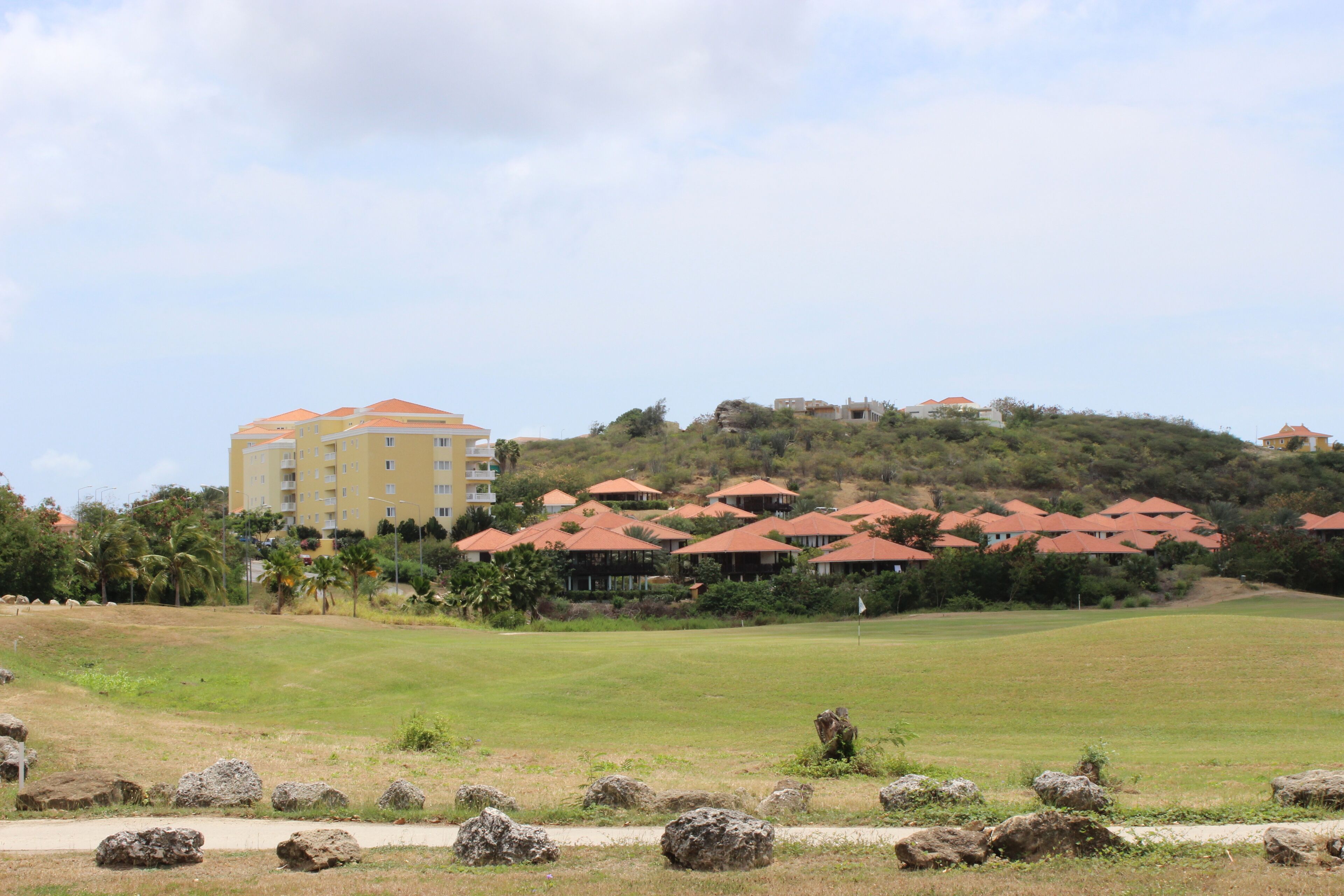 A resort with multiple buildings, a grassy area, and a hilly backdrop.