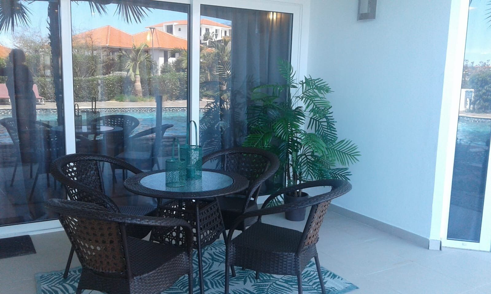 A balcony with a round table and chairs, a potted plant, and a view of buildings and trees.