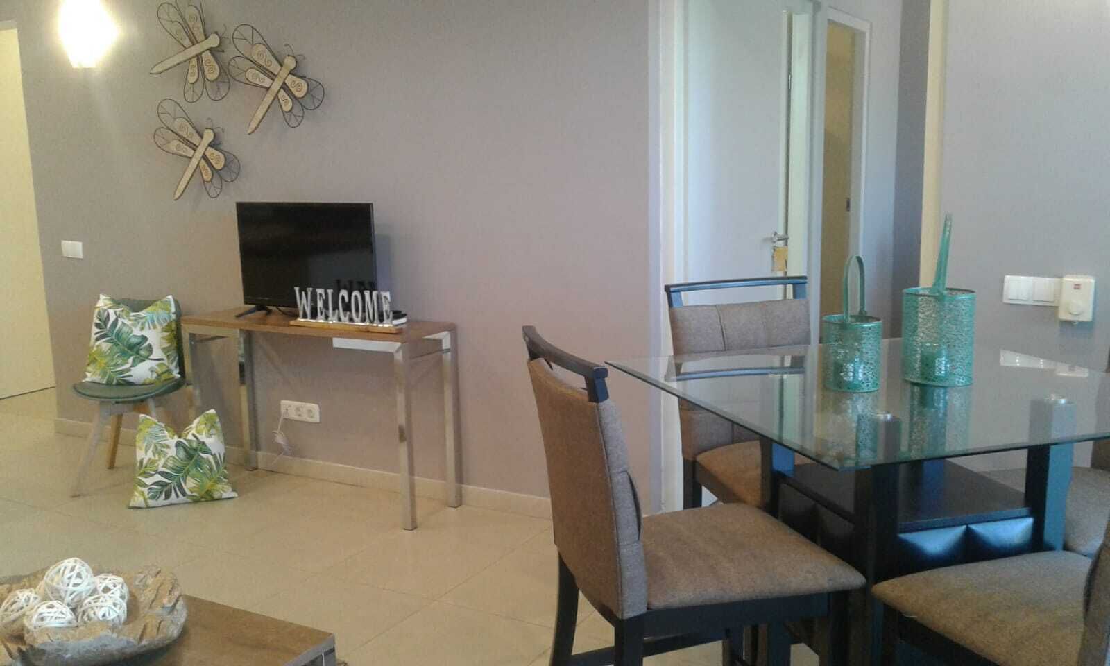 A modern living room with a glass dining table, comfortable seating, a TV, and decorative wall art.