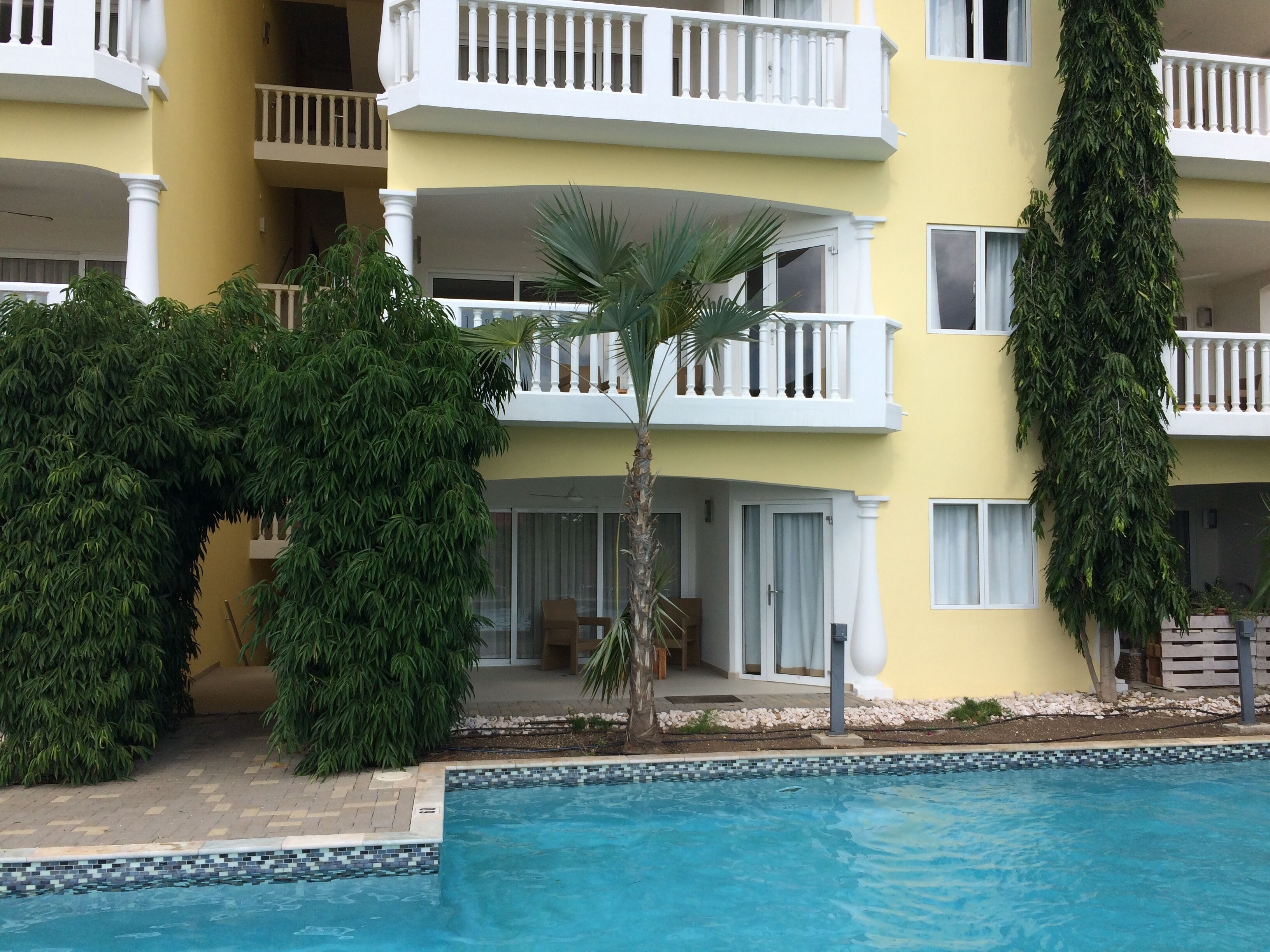 A hotel with a pool, a palm tree, and a yellow facade.