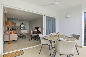 A modern dining area with a round table, chairs, and a view of the kitchen and living room through an open door.