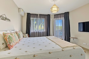 A bedroom with a bed, curtains, a hanging light fixture, and a television.