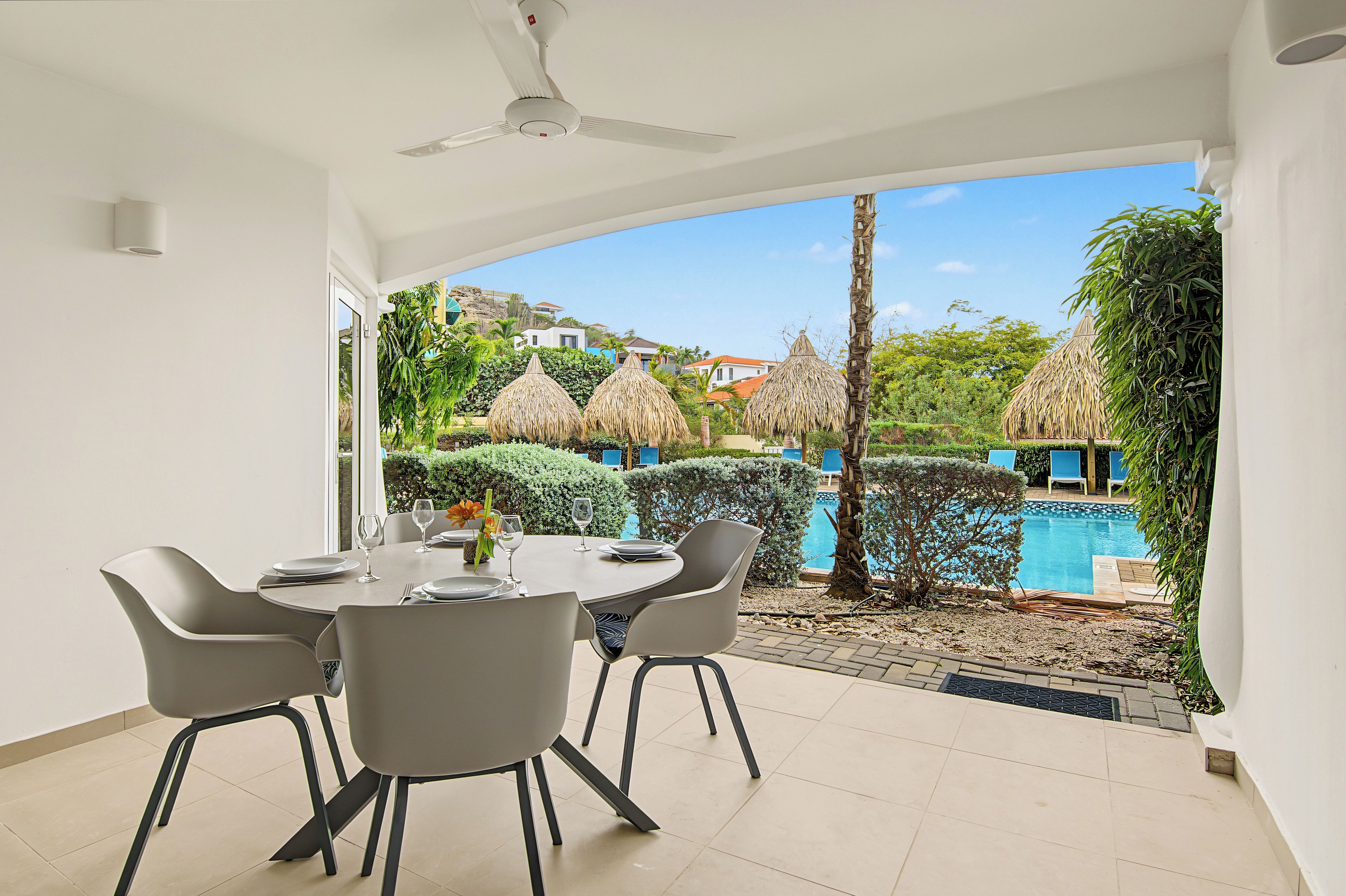 Un coin repas avec une table dressée pour quatre personnes, donnant sur une piscine et une végétation luxuriante.