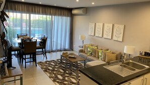 Un soggiorno moderno con zona pranzo, cucina con lavello e un'ampia finestra con tende leggere.