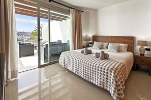 A hotel room with a large bed, two bedside tables with lamps, a sliding glass door to a balcony, and a city view. - Villa Salobre Golfers 1 (Maspalomas)
