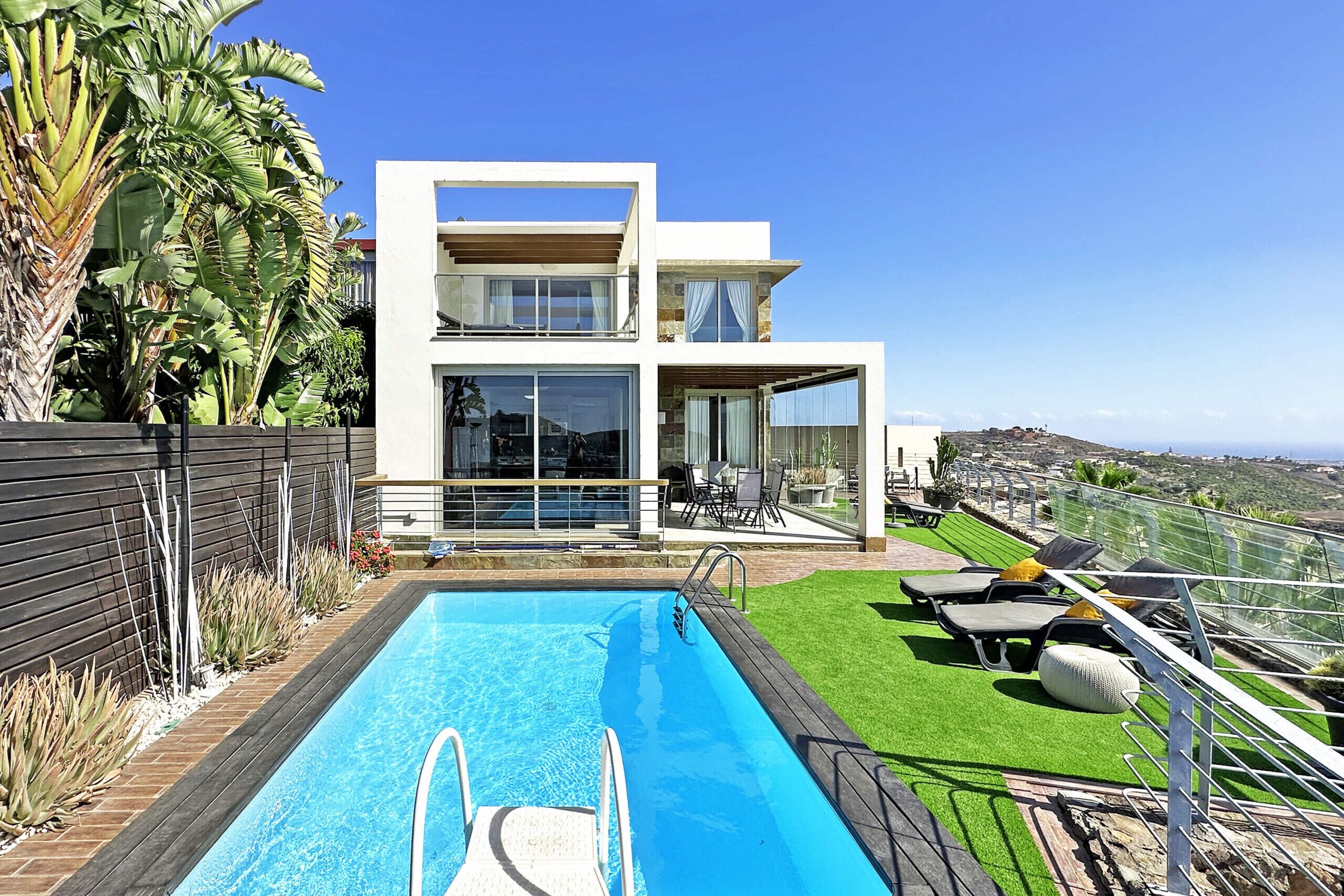 Una casa moderna de dos pisos con piscina, mobiliario de exterior y vistas del paisaje.