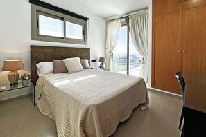 A bedroom with a large bed, a nightstand with a lamp, a wardrobe, and a window with curtains. - Villa Salobre Golfers 1 (Maspalomas)