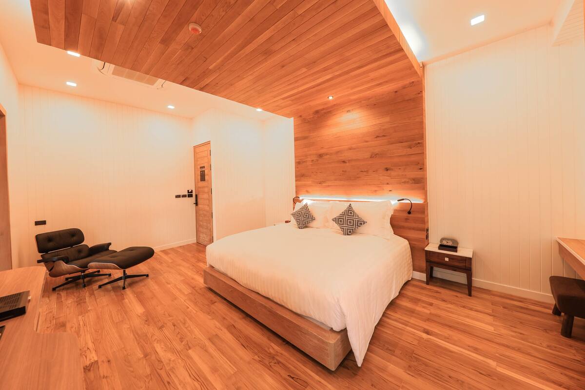 A modern bedroom with a wooden ceiling, a large bed with patterned pillows, a desk, and a chair.