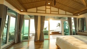 Un dormitorio amplio con una cama grande, techo de madera y vistas al océano a través de puertas correderas de vidrio.