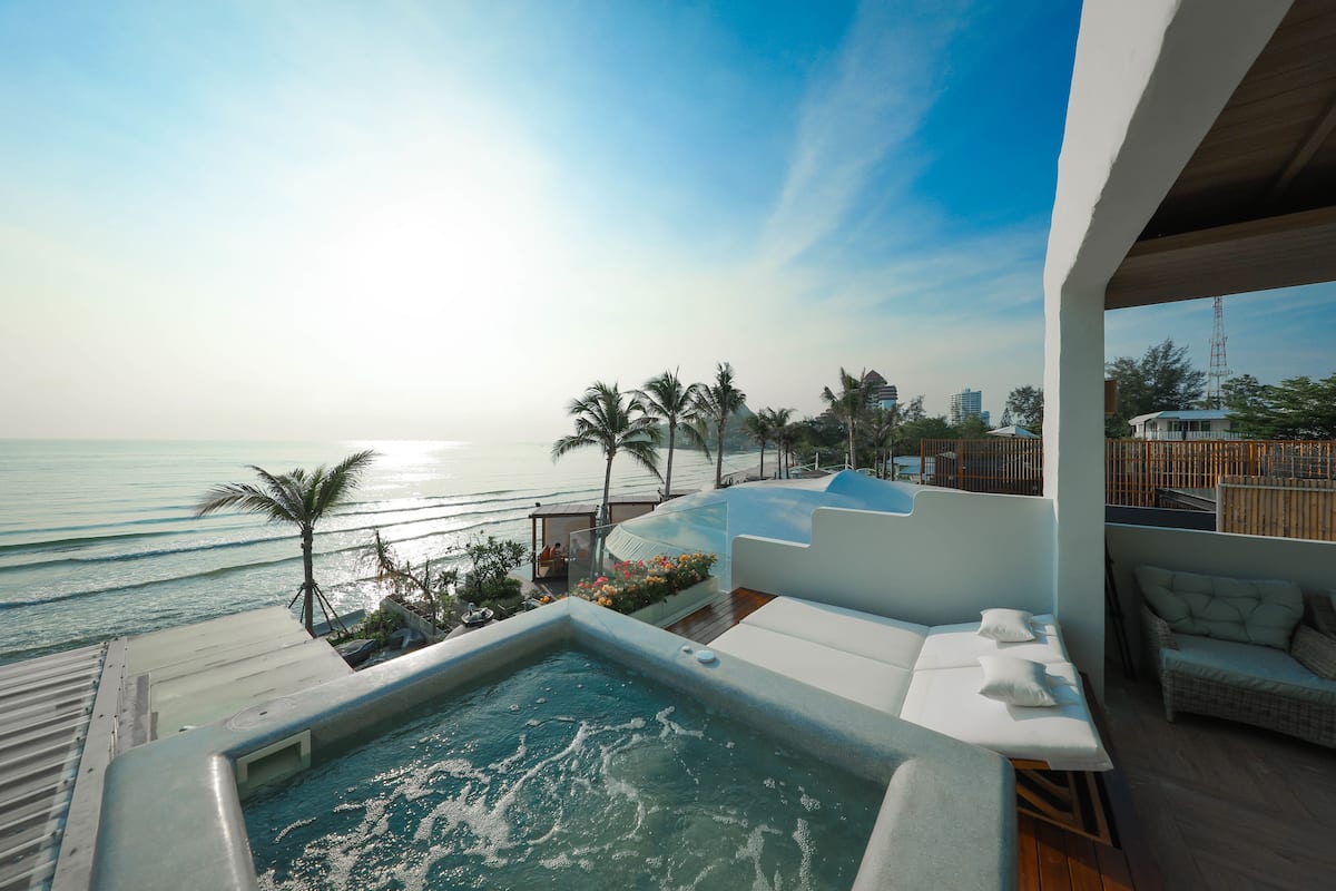 A rooftop pool with a view of the ocean, palm trees, and a modern building in the background.