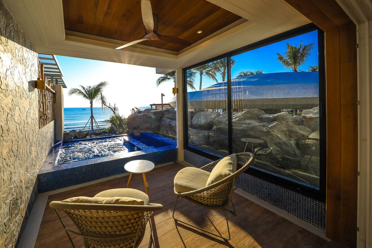 A modern room with a large window, a ceiling fan, a small pool, and two wicker chairs.